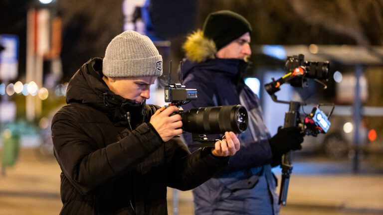 Operatőrök éjszakai céges videó készítés közben, kézi stabilizátorral és teleobjektíves kamerával
